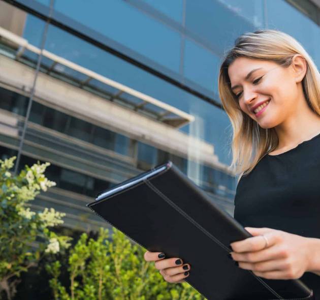 Business woman holding clipboard and standing outdoors.