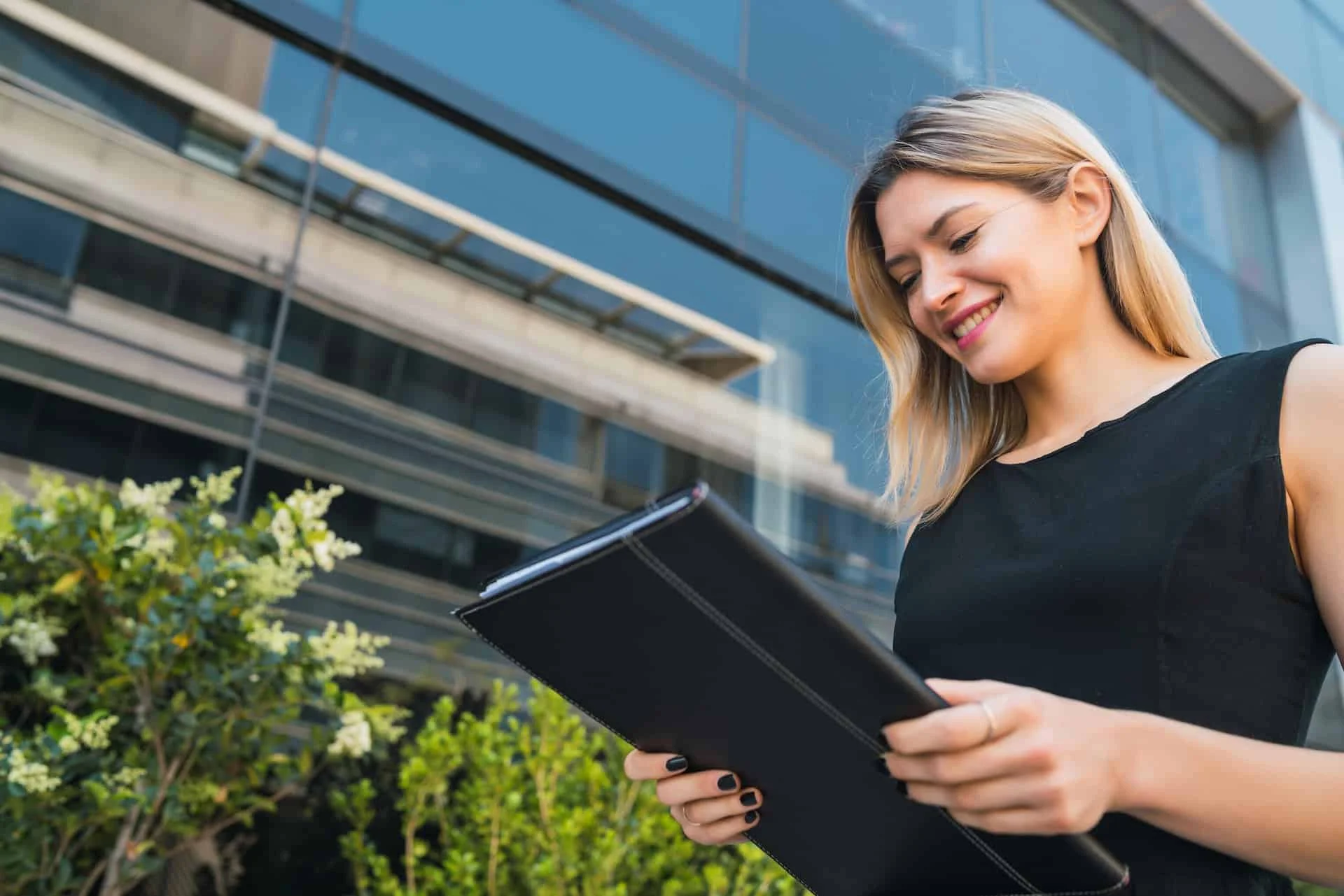 Business woman holding clipboard and standing outdoors.